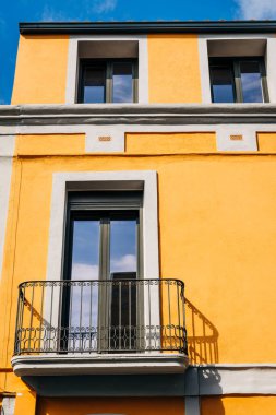 Güneşli bir günde açık mavi gökyüzünün altında canlı sarı bir bina, şehir mimarisini gözler önüne seriyor.