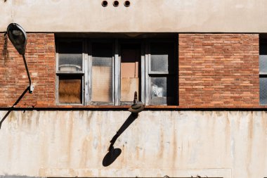 Kentsel Çürüme: Açılmamış Pencereler ve Yıpranmış Tuğla Duvardaki Yalnız Lamba. Mimari terk edilme ile kentsel bir ortamda zamanın esnekliği arasındaki mutlak zıtlık