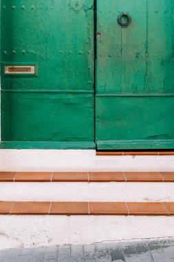 Pürüzsüz beyaz duvarlara ve terakotta basamaklarına zıt eski, yıpranmış yeşil bir kapı geleneksel Akdeniz tarzını çağrıştırıyor.