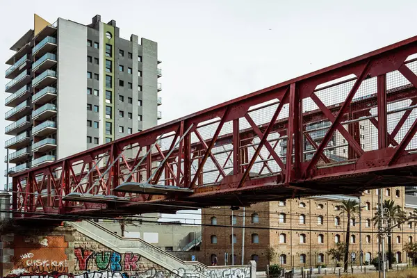 Badalona, İspanya-1 Ocak 2025 Badalona, İspanya 'da modern ve tarihi binalar, duvar yazıları ve altında demiryolu rayları olan kırmızı bir yaya köprüsü..