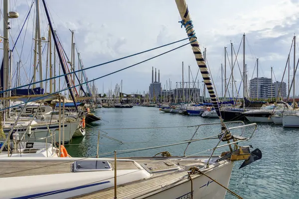 Badalona, İspanya - 30 Aralık 2024. İspanya 'nın Badalona limanında demirlemiş yelkenlilerin modern binaları ve bulutlu bir gökyüzünün altında sakin suları olan yakın görüntüsü...