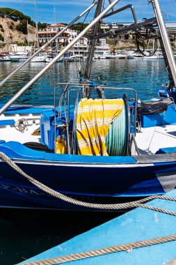Mavi bir balıkçı teknesi marinaya yanaşmış. Üzerinde sarı çizgili muşamba var..