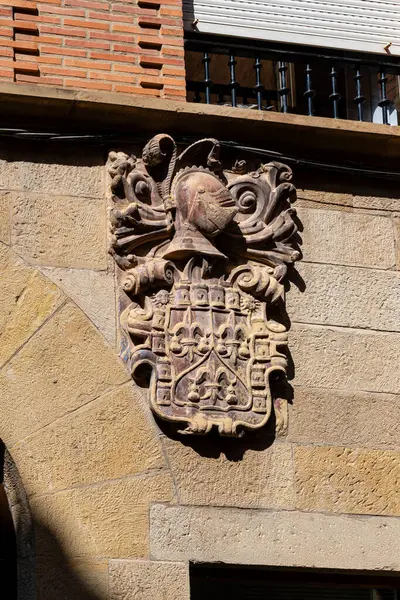 Tarihi bir taş bina cephesine ortaçağ arması monte edilmiş. Ayrıntılı heykel bir şövalye miğferinin sağa bakmasını içeriyor.