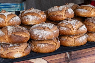 Bir market tezgahına istiflenmiş taze pişmiş yuvarlak ekmek somunları, kabuklu altın kabuk ve hafif un tozlu.