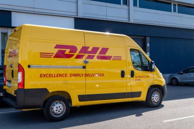Montgat, İspanya-21 Haziran 2025. Parlak sarı DHL minibüs, güneşli bir öğleden sonra şehir teslimatına hazır modern bir binanın önüne park edilmiş..