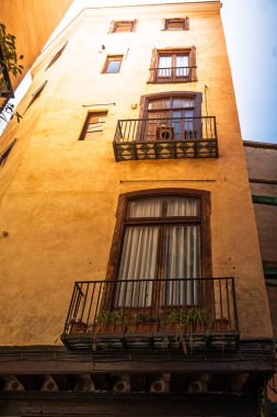 Barselona, İspanya 'nın gotik bölgesinde balkonları ve bitkileri olan bir konut binasının ön cephesini aydınlatan güneş ışığı.