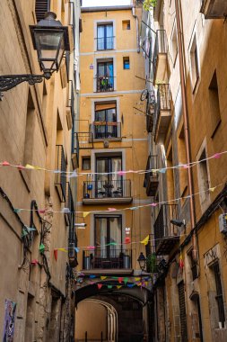 Barselona, İspanya-21 Nisan 2025. Barselona 'nın Barri Gtic bölgesindeki dar bir sokakta tarihi sarı binalar ve kemerli bir yol...