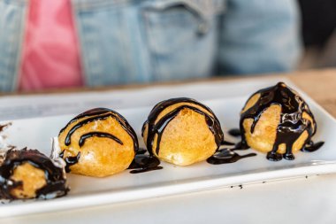 Çatal, kremayla dolu ve çikolata sosuyla kaplı profiterolden bir ısırık alıyor.