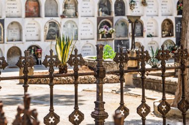 Barselona, İspanya-17 Ağustos 2025. Ön planda paslanmış demir çitleri olan tarihi mezarlık, parlak güneş ışığı altında çiçeklerle süslenmiş, yer üstü mezarlarını gösteriyor..