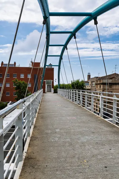Turkuaz kemerler ve çelik kablolarla modern bir yaya köprüsünün beton geçidi, kentsel bir çevrede binaları birbirine bağlıyor, Badalona, İspanya