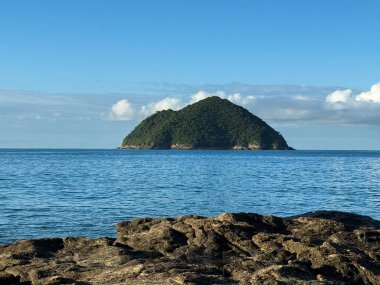 Berrak bir gökyüzünün altında sakin mavi sularla çevrili uzak yeşil bir adanın sakin bir görüntüsü. Engebeli, kayalık ön plan resim sahnesine derinlik katıyor. Huzur ve yalnızlık hissi uyandırıyor..