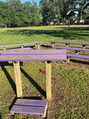 Çimenli bir sahanın ortasında mor banklarla çevrili renkli ahşap bir podyum. Sahne, açık mavi gökyüzünün altında arka planda basketbol sahaları olan bir açık hava parkında geçiyor..