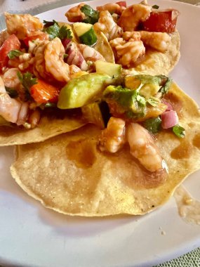 İçlerinde avokado, domates, soğan ve turunçgil salamurasında kişniş bulunan canlı karides ceviche ile kaplı üç çıtır tostada. Beyaz tabakta renkli ve ferahlatıcı bir deniz ürünleri aperatifi..