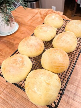 Taze pişmiş mayalı hamurlar soğutma rafında, arka planda yeşillik, ahşap tezgahta kahverengi un tozu ve ekmek.