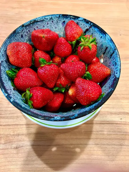 Benekli mavi bir seramik kasede taze kırmızı çilek manzarası. Kase beyaz bir tabakta duruyor. Tahta bir yüzey üzerinde yeşil bir halka var..