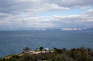 Yunanistan 'ın orta Moreloponese kıyı şeridi boyunca manzaralı bir vanLife durağı. Deniz kenarında bir karavan var. Mavi suların ve uzak dağların çarpıcı manzarası var..