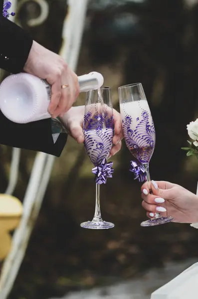 Gelin ve damadın iki eli bardakta bir buket beyaz şarapla.