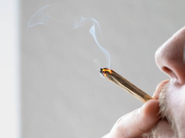 Yakın planda esrar içiyorum. Sigaranın dumanını esrarla solumak. Genç bir adam ışıldayan eklemleri ağzına dayayıp tadını çıkarıyor..