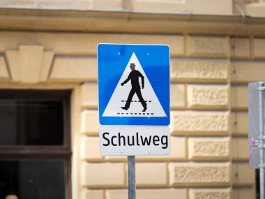 Schulweg (okul trafik işareti) Avusturya 'da. İşarette Almanca yazıyor. Okul binasının yanından yaya geçidi. Yaya geçidine dikkat et..