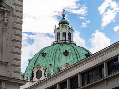 VIENNA, AUSTRIA - 28. Temmuz 2024: St. Charles Kilisesi (Karlskirche) kubbesi diğer binaların arkasında. Altın elementli yeşil bronz çatı. Avusturya 'nın orta kesimindeki Viyana' da barok tarzı mimari.