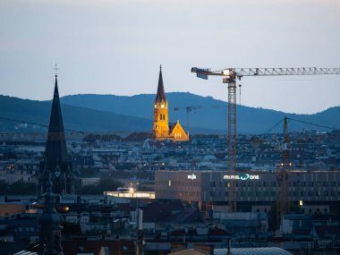 VIENNA, AUSTRIA - 31. Temmuz 2024: Katolik Kilisesi Rudolfsheim şehir manzarasında. Tarihi bina, akşam saatlerinde aydınlanmaktadır. İbadet yeri ve seyahat yeri.