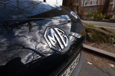 DRESDEN, ALMANY - 12. Nisan 2025: MG amblemi yakın çekim görüntüsünde. Çin elektrikli arabasının dış tarafında marka logosu. Ön kaputtaki teknoloji ve otomotiv şirketinin kimliği..