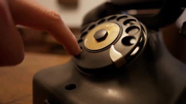 Çevirmeli telefon kullanarak ve numarayı çevirerek. Geçmişten kalma eski bir siyah iletişim cihazı. Yakın planda antika bir telefon..