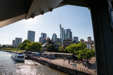 FRANKFURT, Almanya - 13. Mayıs 2025: Finans bölgesi ve Demir Köprü 'den ana nehir manzarası. Turnuva teknesi turistler için bir cazibe merkezi. St. Leonhard kilisesi görülebilir..