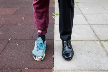 Zenginlere karşı fakir. Takım elbiseli zengin bir iş adamı yırtık pırtık elbiseli bir evsize karşı. Farklı pantolonlar ve ayakkabılar. Toplumda ve sınıf mücadelesinde karşıtlık. Başarısızlığa karşı başarı kavramı.