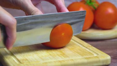  Bambu kesme tahtasındaki domates dilimlenmeye hazır, arka planda üç tane olgun kırmızı domates var.