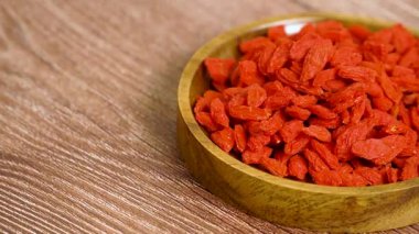 Canlı kırmızı goji üzümleriyle dolu dönen ahşap bir tabağın yan görüntüsü, özelleştirilebilir içerik yerleştirme için yerleştirilmiş