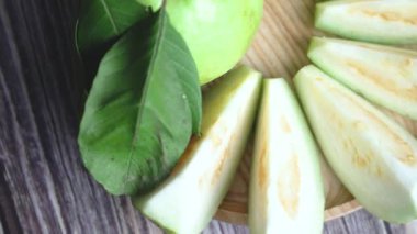 Guava 'nın bir tabağının baştan aşağı yakın plan görüntüsü, tam bir guava ve ortada düzgünce düzenlenmiş dilimlerle çevrili yapraklar.