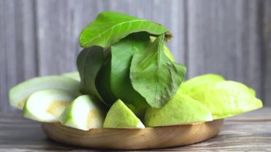 Guava 'nın dönen bir tabağının tam bir guava ile yakın plan görüntüsü ve ortada düzgünce düzenlenmiş dilimlenmiş parçalarla çevrili yapraklar.