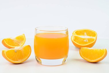 Cam bardakta portakal suyu ve arka planda portakal dilimleri.