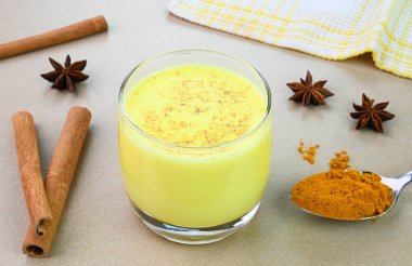 Cam bardakta zerdeçal sütü ve arkaplanda zerdeçal tozu ve tarçın var.