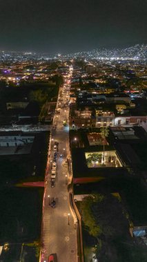 İnsansız hava aracı fotoğrafı Oaxaca, Meksika 'daki Xochimilco mahallesinin büyüleyici gece hava görüntüsünü yakalıyor ve arka planda ışıklar yanıp sönüyor. Aydınlatılmış sokaklar ve kenar mahallelerin sömürge mimarisi görülebilir durumda.