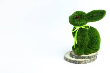 Yeşil kurdeleli yosun kaplı tavşan heykelciği tahta dilimler üzerinde, beyaz üzerinde izole bir şekilde oturuyor. Paskalya, bahar dekorasyonu ve çevre dostu veya kırsal görsel temalar için ideal.