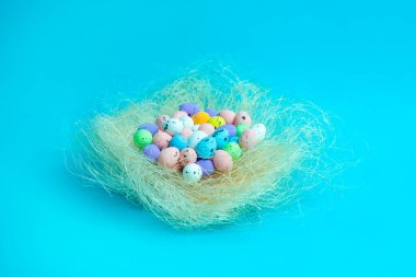 Benekli pastel Paskalya yumurtaları, parlak mavi bir arka planda saman yuvasında. Bahar temalı tasarımlar, tebrik kartları, festival reklamları, sosyal medya içeriği veya mevsimlik dekorasyonlar için ideal.