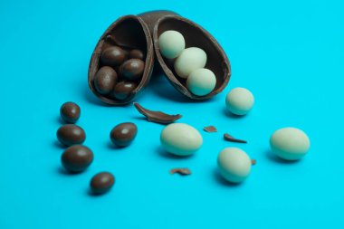 Kırık bir Paskalya yumurtası parlak mavi bir zemin üzerine süt ve koyu çikolata şekeri döker. Bayram temalı pazarlama ve reklamcılık için mükemmel bir yiyecek konsepti..