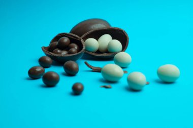 Kırık bir Paskalya yumurtası parlak mavi arka planda süt ve beyaz çikolata kaplı şekerlerin karışımını ortaya çıkarır. Lezzetli ve şenlikli bir kompozisyon. Yemek ve tatil pazarlaması için mükemmel..