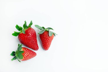Beyaz arka planda yeşil yapraklı üç taze çilek. Canlı ve minimalist bir görüntü gıda pazarlama, sağlıklı yeme kavramları, organik üretim promosyonu ve tasarım projeleri için idealdir..