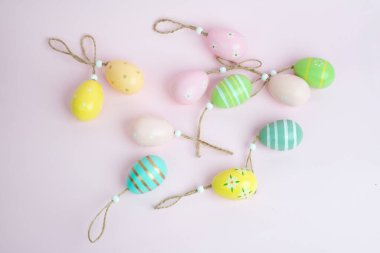 Pastel renkli Paskalya yumurtası süslemeleri. Çiçekli ve çizgili desenleri var. Kırsal sicimle bağlanmış, yumuşak pembe arka planda. Tatil ve şenlikli tasarımlar için mükemmel.