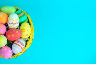 Renkli Paskalya yumurtalarıyla dolu parlak sarı bir sepet kalın bir turkuaz arka plana karşı, bahar kutlamaları için mükemmel neşeli ve neşeli bir bayram teması yaratıyor..
