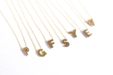 Zarif zincirler üzerinde zarif harfler bulunan altın ilk kolyeler. Minimalist altın harfli kolyeler beyaz bir arkaplanda düzenlenmiş. Kişiselleştirilmiş mücevher severler ve şık moda tasarımları için mükemmel.