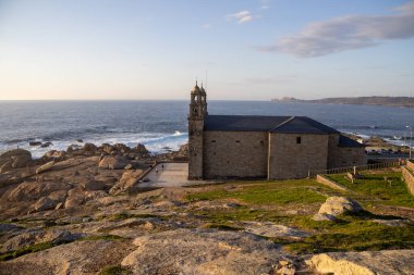 İspanya 'nın Muxa kentindeki A Virxe da Barca' nın mabedi dramatik Atlantik uçurumlarına tünedi. Camino de Santiago 'da önemli bir durak. Gün batımı.