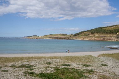Praia de Lourido 'daki Atlantik kıyıları, Muxa, Galiçya, İspanya. Yumuşak kumullar, sakin deniz ve kıyıya giden yeşil bir patika içeren panoramik sahil manzarası.