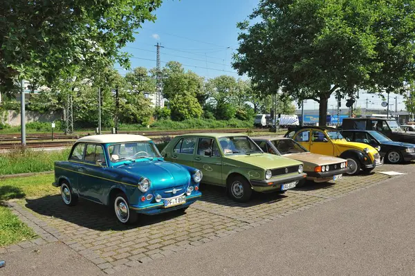 Muhlacker Almanya Mai 18, 2025 Fotoğraf sokağa park etmiş eski arabaları gösteriyor. Ön planda dört farklı renkte araba vardır: mavi, yeşil, kahverengi ve sarı. Arka planda ağaçlar ve demiryolları var..