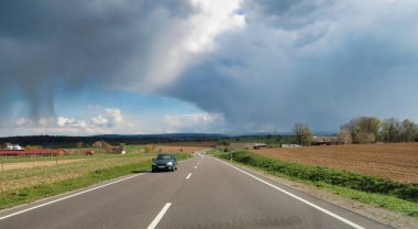 Bulutlu bir gökyüzünün altında çiçek açan ağaçlar ve yeşil tarlalarla dolu dolambaçlı bir yol. Yürüyüş ya da manzaralı sürüş için mükemmel bir yer..
