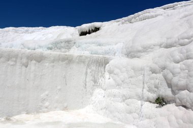 Büyüleyici bir doğa harikası, beyaz teraslar çağlayarak aşağı iniyor, berrak mavi gökyüzünün altında akan su ve mineral yataklarının nefes kesici bir sahnesini oluşturuyor.