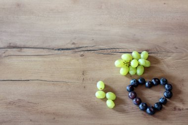 Yaban mersininden yapılmış bir kalp, küçük bir demet yeşil üzümün yanında, ahşap bir yüzeyde oturur ve basit ve sağlıklı bir besin düzeni oluşturur.